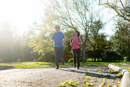Setting a positive example, the elderly couple maintains healthy habits with a light jog in the park, promoting cardiovascular health and vitality through regular exercise.