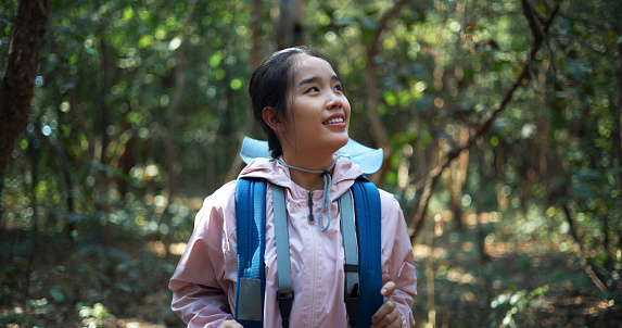 Young Asian backpacker woman walking  and standing breathes fresh air, and looking around, smile with happy at beautiful nature in forest