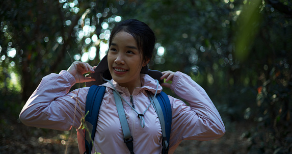 Happily Young Asian backpacker woman walking alone, ,standing and  looking around, she smile with beautiful nature in forest