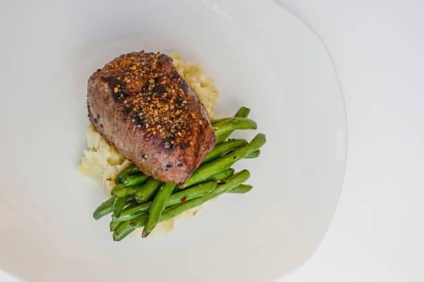 A perfectly cooked Filet Mignon accompanied by green beans, elegantly presented on a bed of mashed potatoes.