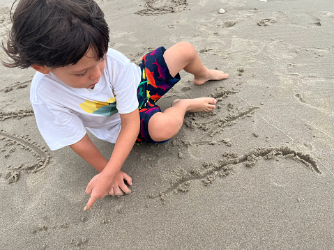Little boy writing with finger in the sand on the beach
