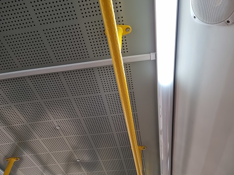 View of a clear bus ceiling with yellow handrails and loudspeaker. Public transport