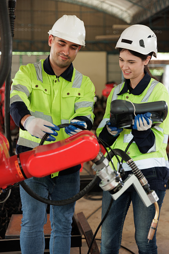 Female engineer controlling robot arm at factory. She checking the operation of robot arm. Technology, automation, innovation and engineering concept.