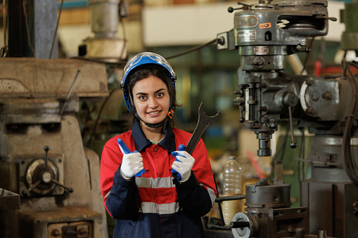 Portrait of professional woman engineer in blue hardhat standing and holding hammer working in factory.