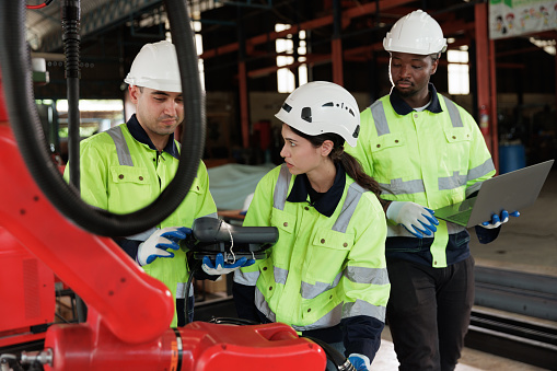 Female engineer controlling robot arm at factory. She checking the operation of robot arm. Technology, automation, innovation and engineering concept.