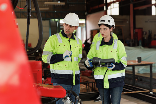 Female engineer controlling robot arm at factory. She checking the operation of robot arm. Technology, automation, innovation and engineering concept.