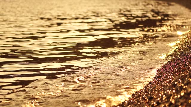 Abstract sea summer ocean sunset nature background. Small waves on golden water surface in motion blur with golden bokeh lights from sun. Holiday, vacation and recreational concept. Nobody Slow motion