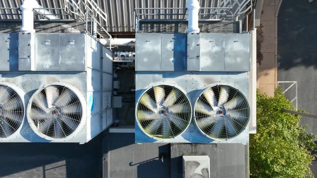Top down aerial of spinning ventilation AC units on rooftop. Industrial HVAC units with fans on a building roof.