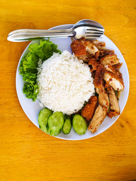 istock Vertical image of crispy fried chicken with basil leaves sprinkled on steamed rice on a plate at a dining table. 1974368977