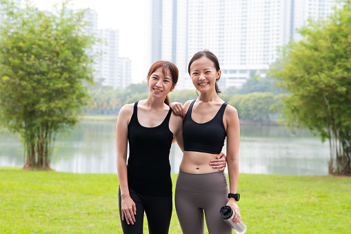 Portrait of two young Asian friends in sport clothing take a short break after exercise workout in public park. Sport Activity, Exercise and Healthy Lifestyle, Healthier, Longer and Better Lives Concepts.