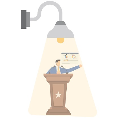 A bright light is focused on a businessman standing on the podium giving a speech