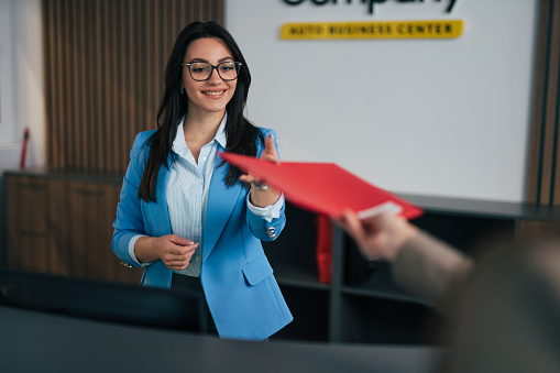 Young businesswoman giving her colleague red folder with financial reports