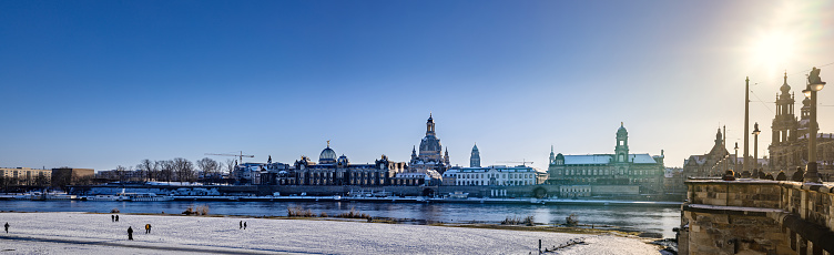 Panoramic view of Dresden historic center from the Elbe River bank during a snowy cold winter day with clear skies and the afternoon sun shinning.