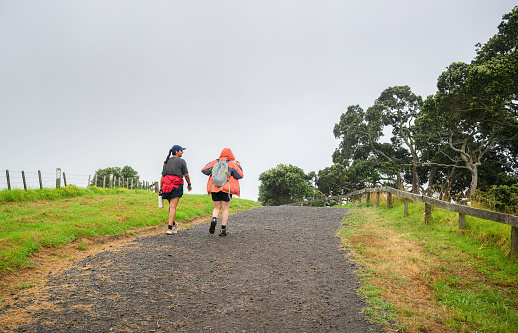 Two women walking the Long Bay coastal Okura Track in the rain. Auckland.