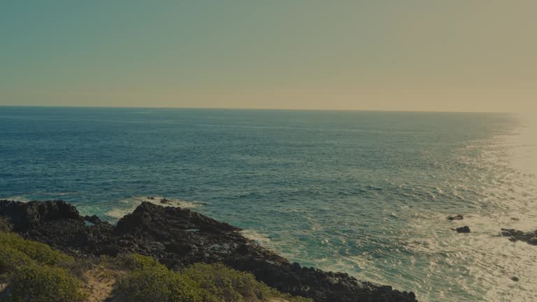 hilltop view of the blue Pacific ocean panning across to see the setting sun reflecting brightly on the ocean water below