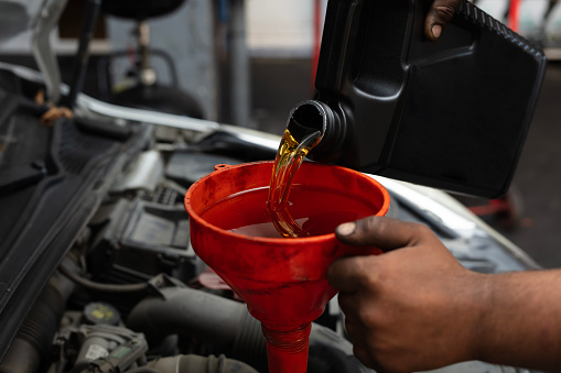 New engine oil pours from canister into motor at car service, close up