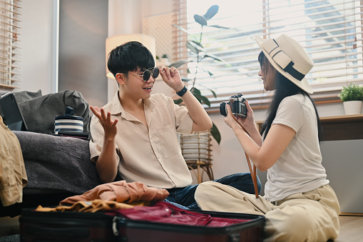 Happy Asian couple packing travel bag for summer vacation in living room. Traveling, vacation and lifestyle concept.