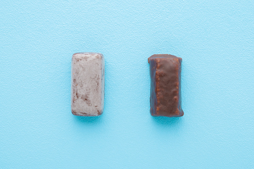 Fresh and old spoiled dark chocolate candies on light blue table background. Pastel color. Compare two pralines. Top down view.
