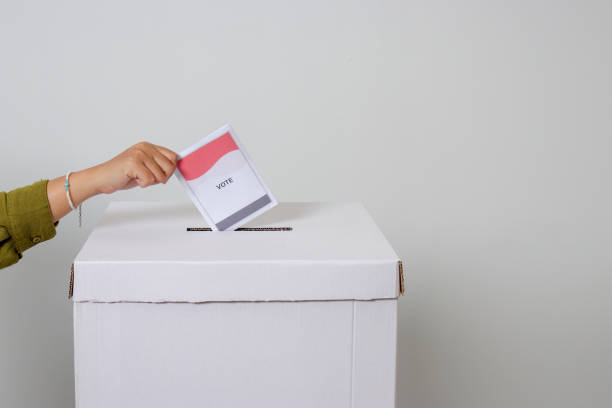 Close up of hand inserting and putting the voting paper into the ballot box. General elections or Pemilu for the president and government of Indonesia. Isolated image on white background stock photo