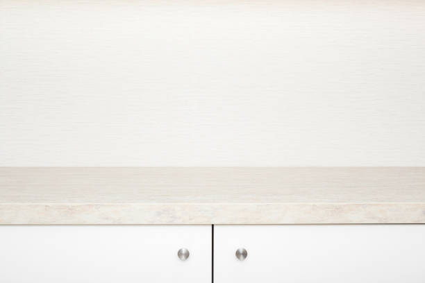 White cabinet doors with stainless handles under stone table top. New kitchen furniture. Closeup. Front view. Empty place for text on beige wallpaper background.