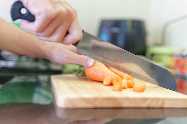 Woman hands cutting fresh orange carrots in a kitchen. Preparing of ripe vegetables. Carrots on a cutting board. Vegetarian healthy food. Product of organic farming.