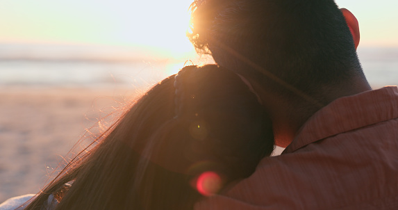 Sunset, beach and back of couple hug in nature for travel, bonding or weekend freedom with lens flare. Sunrise, love and rear view or people embrace at sea for travel, adventure and romance in nature