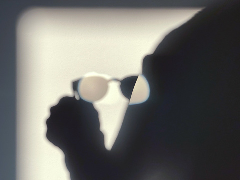 A shadow of a person holding a pair of glasses