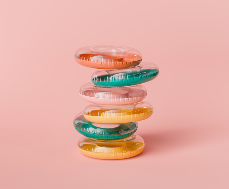 3d rendering of a stack of multicolored inflatable pool rings in orange, teal, yellow, and pink, arranged against a soft pastel pink background. Playful summer concept.