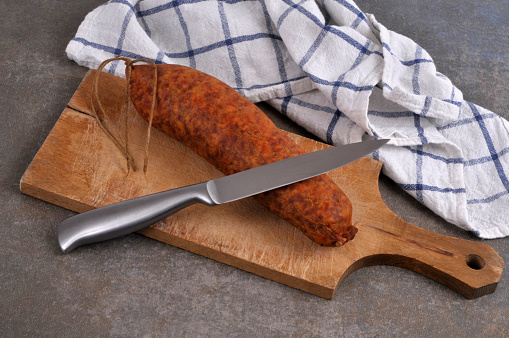 Morteau sausage with a knife on a wooden cutting board on gray background