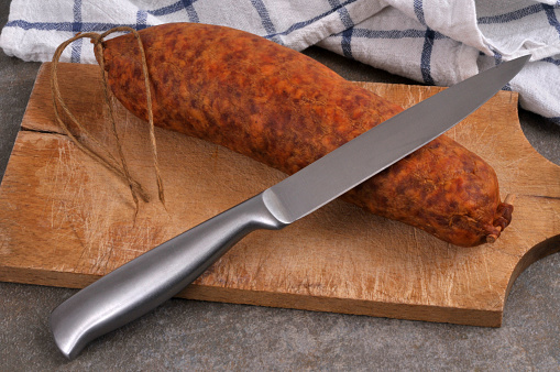 Morteau sausage with a knife on a wooden cutting board closeup