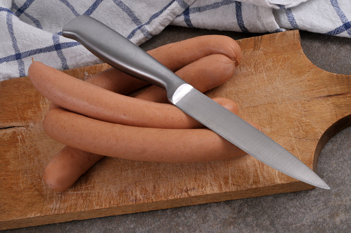 Bundle of frankfurter sausages on a cutting board with a knife close-up