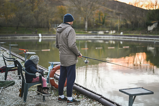 Family in fishing on a pond bank in cold weather.