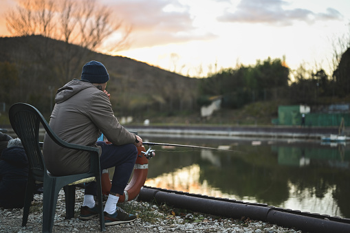 Rear view of a millennial man fishing outdoors in sunset time.