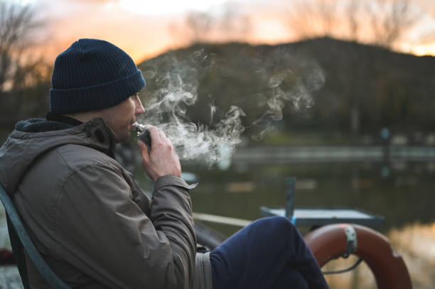 jovem fumando cigarro eletrônico no tempo frio ao ar livre. - quit lake - fotografias e filmes do acervo