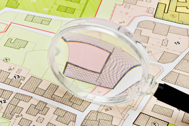 istock Imaginary cadastral map with buildings, land parcel and vacant plot - property registry and real estate concept seen through a magnifying glass - note: the map background is totally invented and does not represent any real place 1974692826