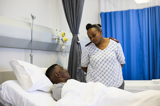 Nurse checks in on senior man lying in bed in hospital ward