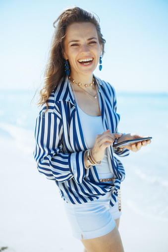 happy stylish 40 years old woman on the seashore with smartphone.