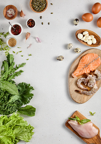 Protein-rich ingredients assortment with fish, chicken, shrimp, cheese, and fresh greens, top view for nutritious meal planning and dieting guides.