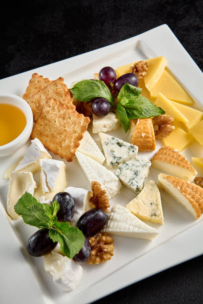 istock Cheese board with grapes and honey on a white plate against a black background 1974736198
