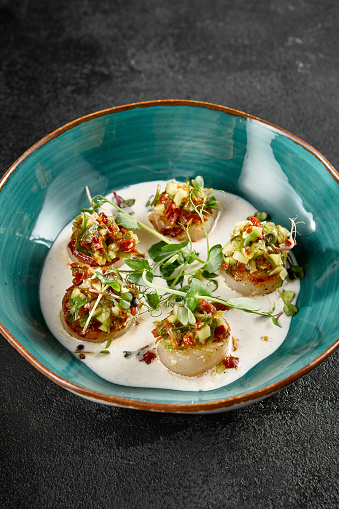 Scallops in a creamy mousse with tomato salsa, delicately plated in a turquoise dish.