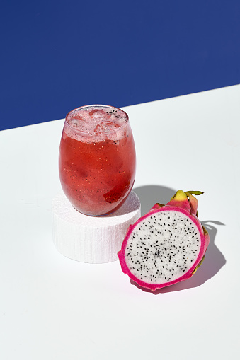 An exotic lemonade with dragon fruit, elegantly perched on a white pedestal, complemented by a bold blue background.