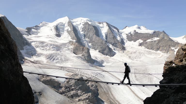 Drone aerial view, Man on an hike in the Alps crosses suspension bridge high above glacier