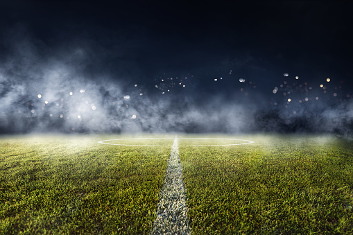 Football kept on grassy football pitch in front of goal post.