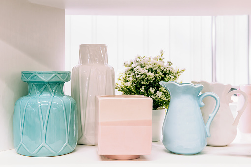 front view of various ceramic vases ceramic concept. Shelves with ceramic dishes in the pottery workshop. A set of clay pots and ceramic dishes, which is stored on a wooden shelf in a pantry with a white wall. Photo of the interior object.