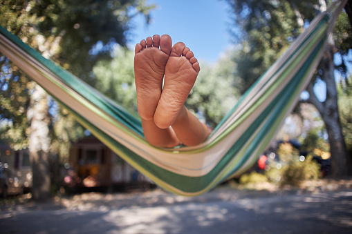 Unrecognizable child enjoying hammock by the tent in nature. Foot in focus. Summer vacation.