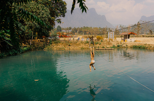 Woman jumping into the tropical  lake from a rope swing