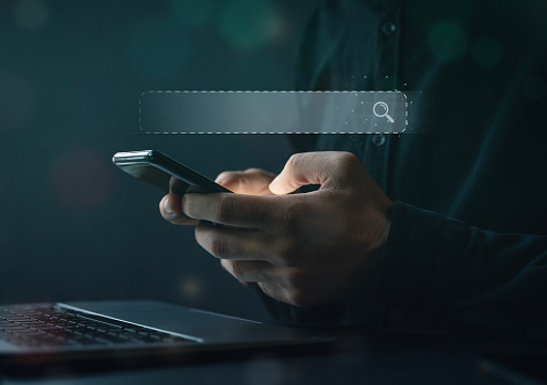 Close-up image of business person's hands using smartphone searching for what they are interested in. Search bar virtual screen