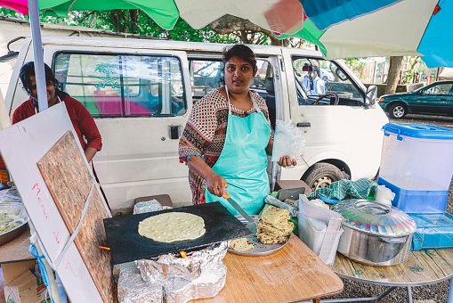 Port Louis, Mauritius - January 12, 2023: A woman standing in front of a table filled with Indian bread and various dishes.