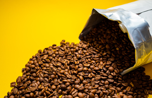 coffee beans poured from the pack on a yellow background