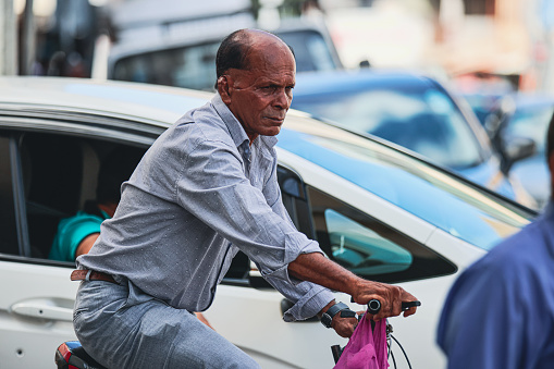 Port Louis, Mauritius - January 12, 2023: A man is seen riding a bicycle down a street lined with parked cars in Mauritius.